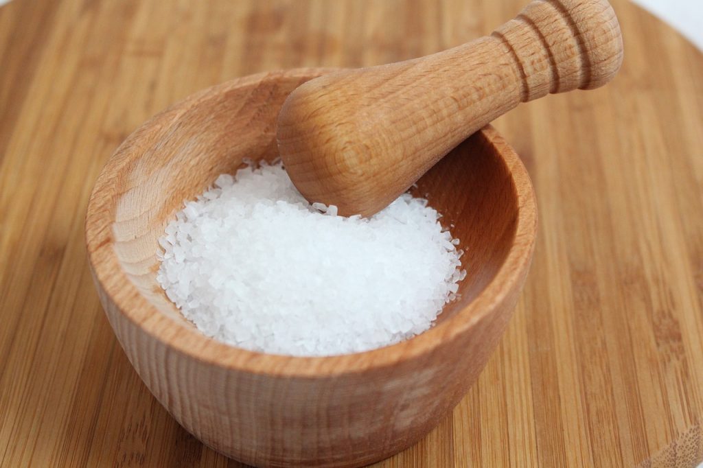 A wooden bowl and scoop filled with sea salt, emphasizing the health benefits of reducing salt intake.