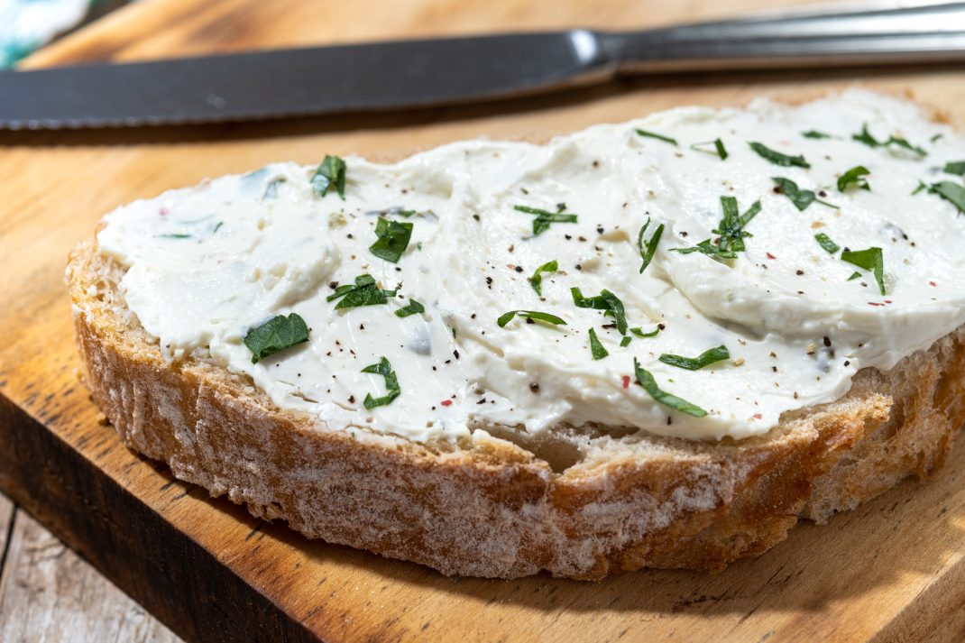 A slice of bread topped with creamy cheese and sprinkled with herbs.