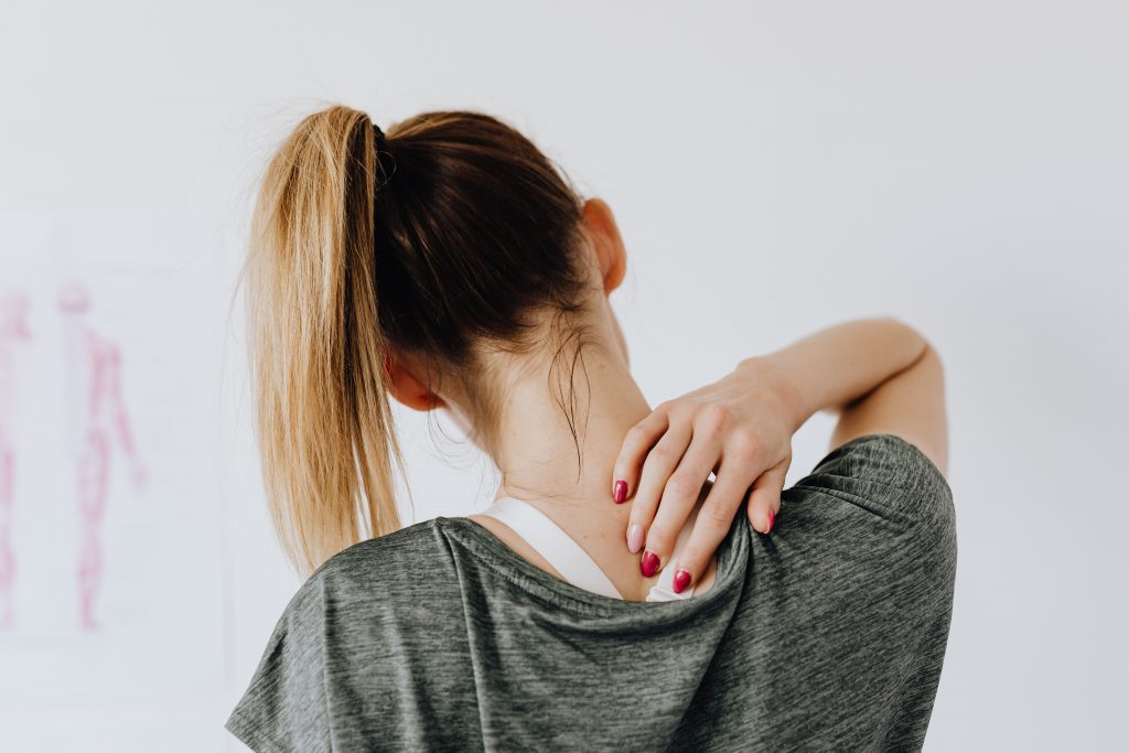 A woman in a gray shirt touching her neck and shoulder, emphasizing the risks of untreated pain causing lasting damage.