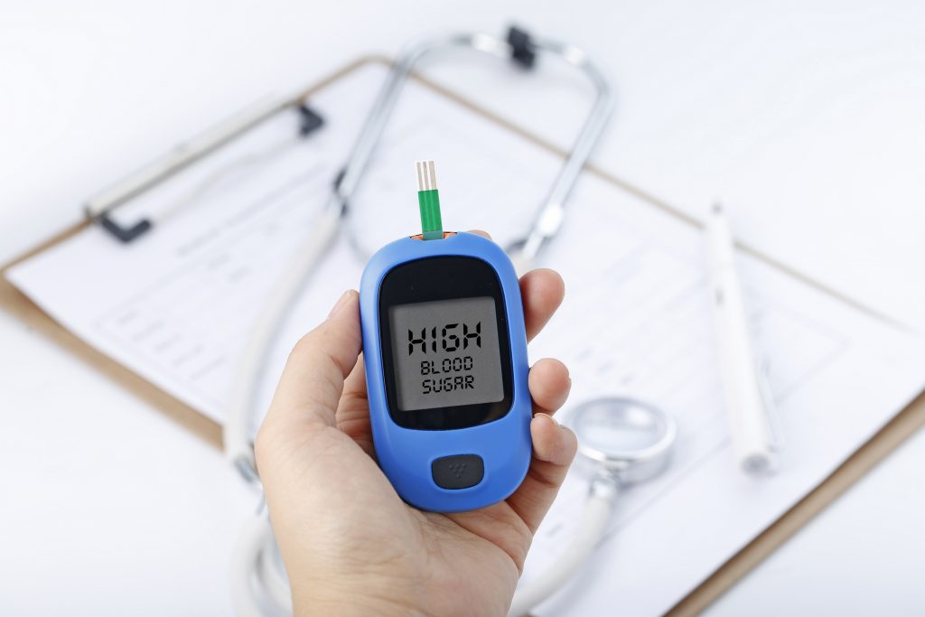 Person holding a glucometer with a stethoscope on the pad, symbolizing diabetes and its impact on blood sugar levels and metabolism.