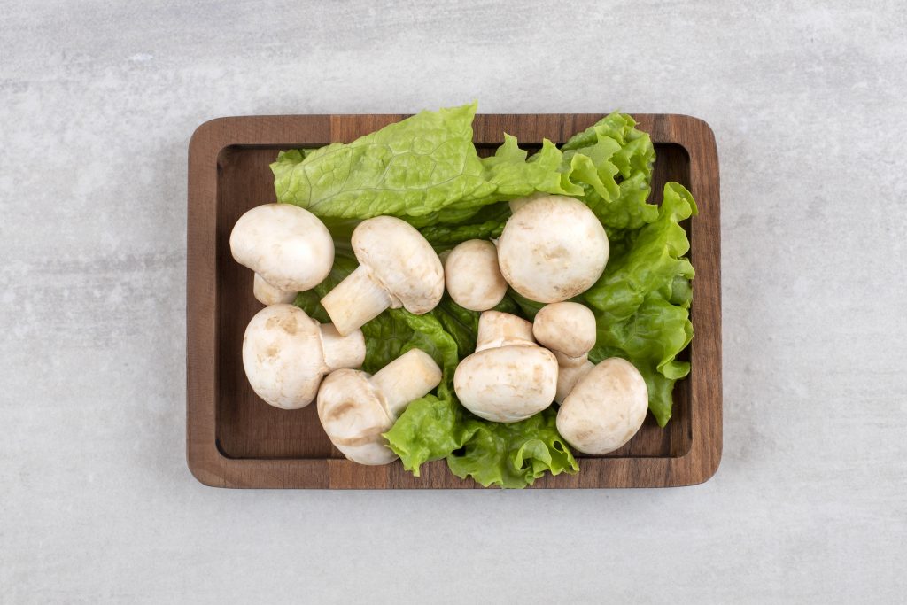 Fresh mushrooms with lettuce on a wooden tray, supporting cognition, heart health, and illness prevention with bioactive chemicals.