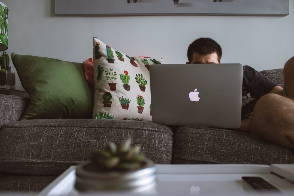 A man working on a laptop on a couch, holding a posture for long hours, leading to overworked muscles.
