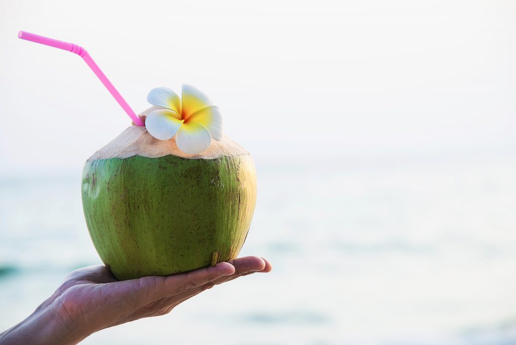 A hand holds a fresh coconut drink with a straw and flower garnish, rich in potassium and perfect for rehydration after exercise.