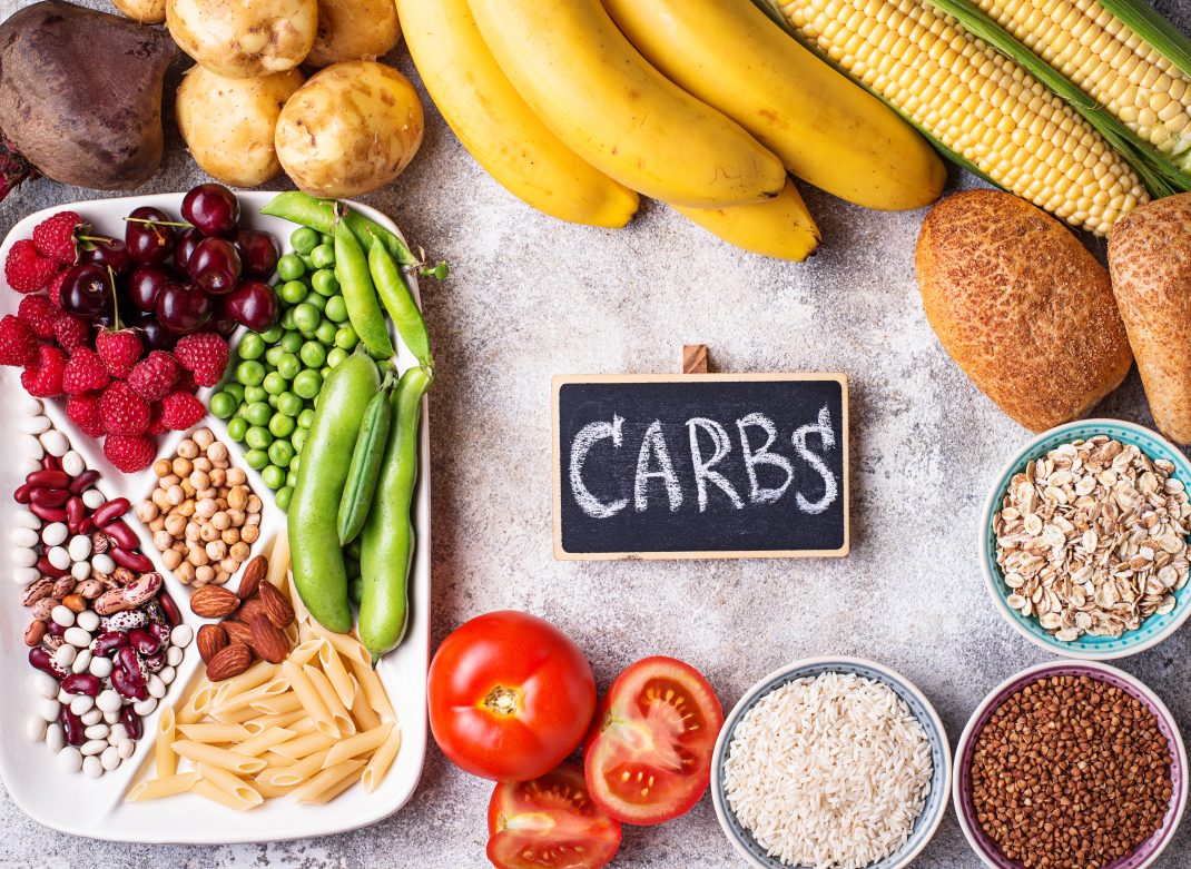 Foods high in complex carbohydrates placed around a wooden plate labeled "CARBS".