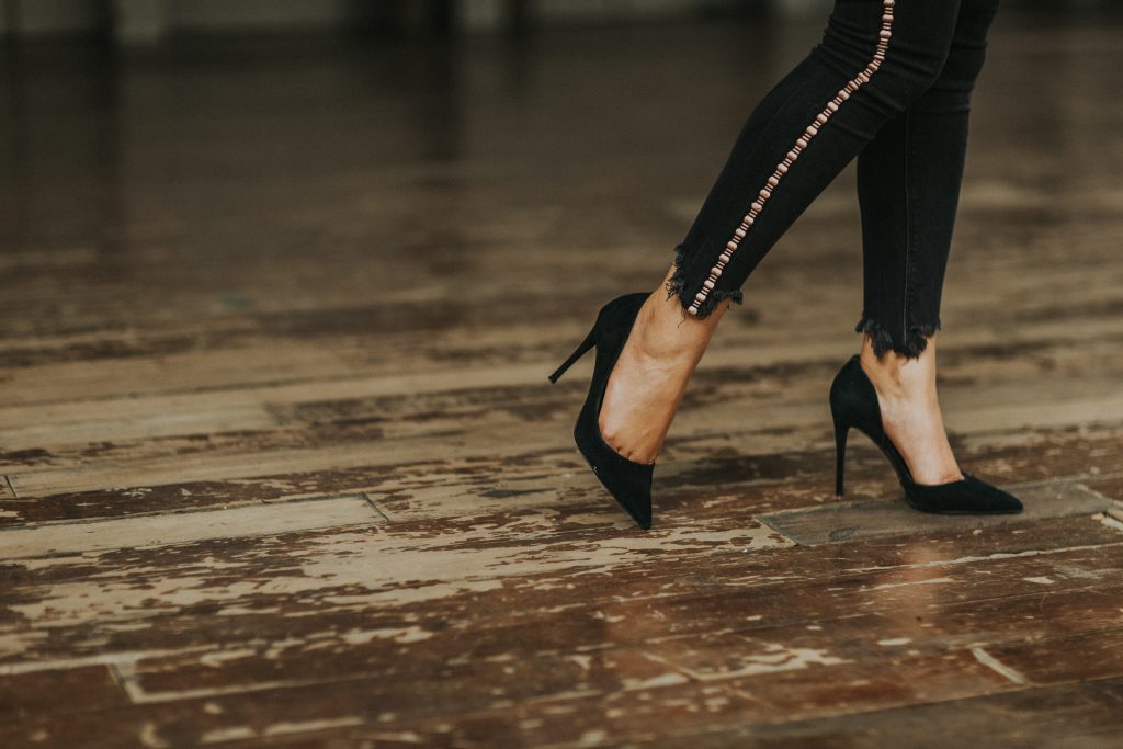 Close-up of a woman's legs in black jeans and high heels, highlighting foot problems, instability, and injury risks.