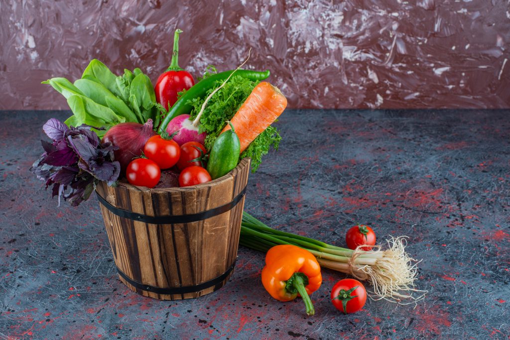 A wooden bucket filled with nutrient-rich vegetables like tomatoes, cucumbers, and leafy greens.