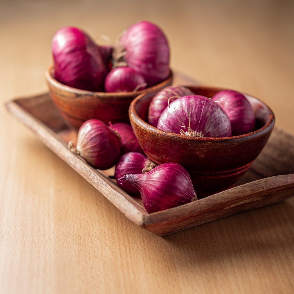 Red onions in wooden bowls on a tray, helping to boost blood flow and support heart health.