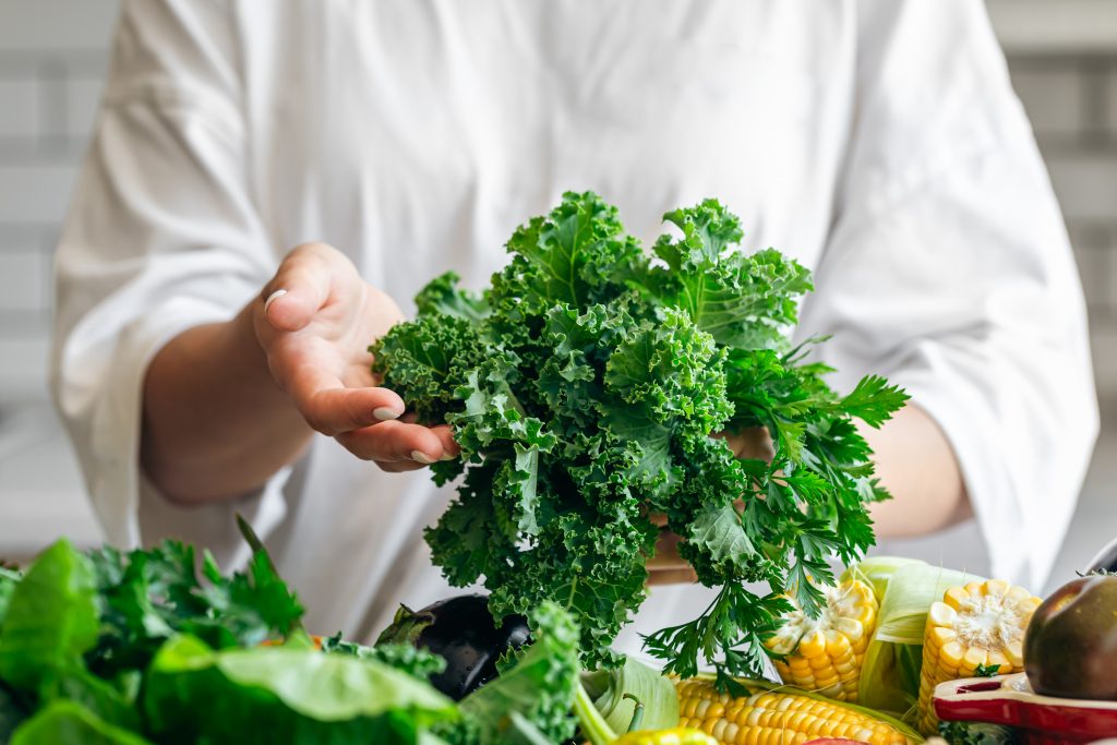 A person holding fresh kale cabbage leaves, surrounded by vegetables, showcasing some of the most nutrient-dense foods.