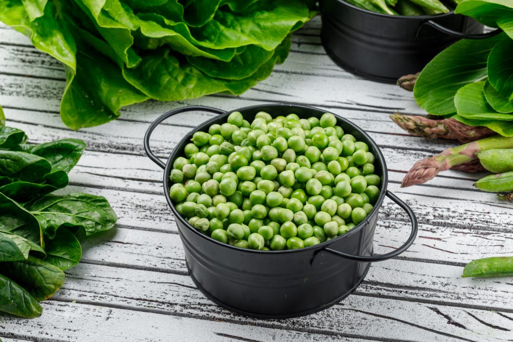 A bowl of fresh green peas on a wooden table, promoting healthy digestion and gut bacteria balance.