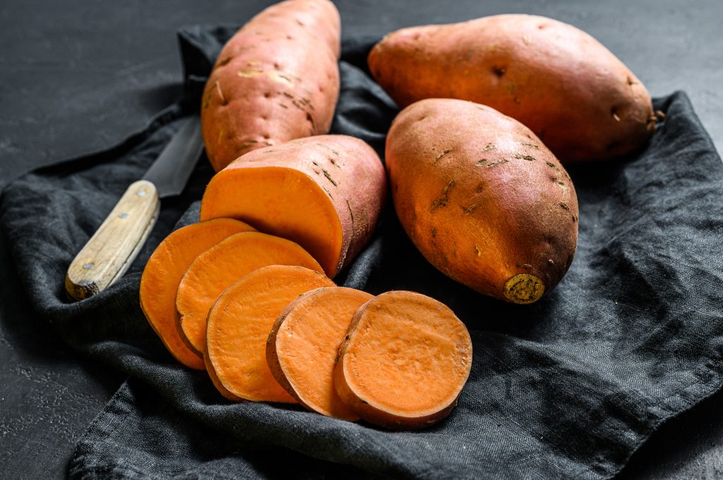 Sweet potatoes, with one sliced and a knife, a healthy choice for managing blood sugar levels in diabetes.