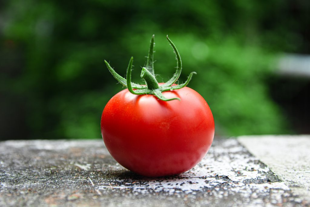 A ripe red tomato with a green stem on a concrete surface, rich in potassium and linked to reduced inflammation and cancer risk.