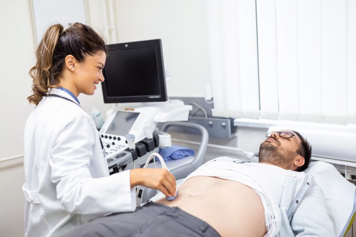 A doctor sitting in front of an ultrasound apparatus and conducting abdominal diagnostics with transducer.