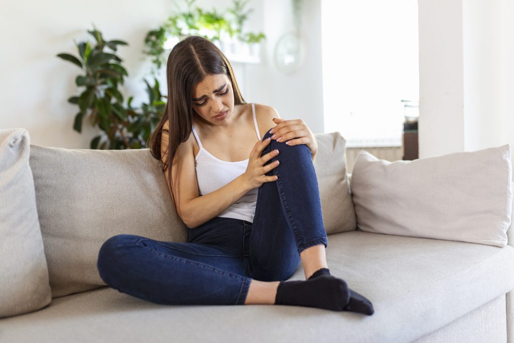 A woman sitting on a couch, holding her knee in pain, reflecting the impact of daily habits bad for your joints.