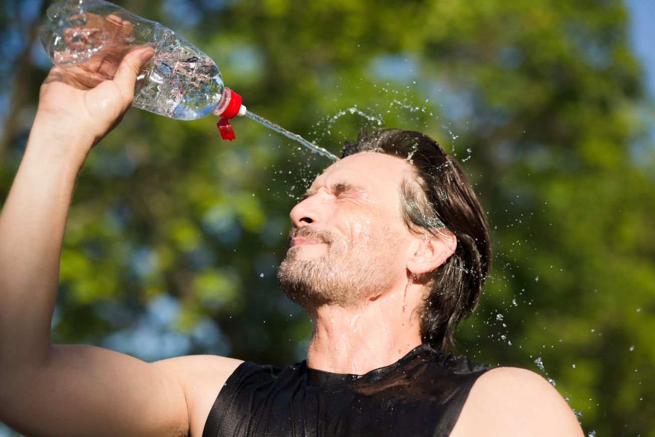 A man splashing water on his face due to heat.