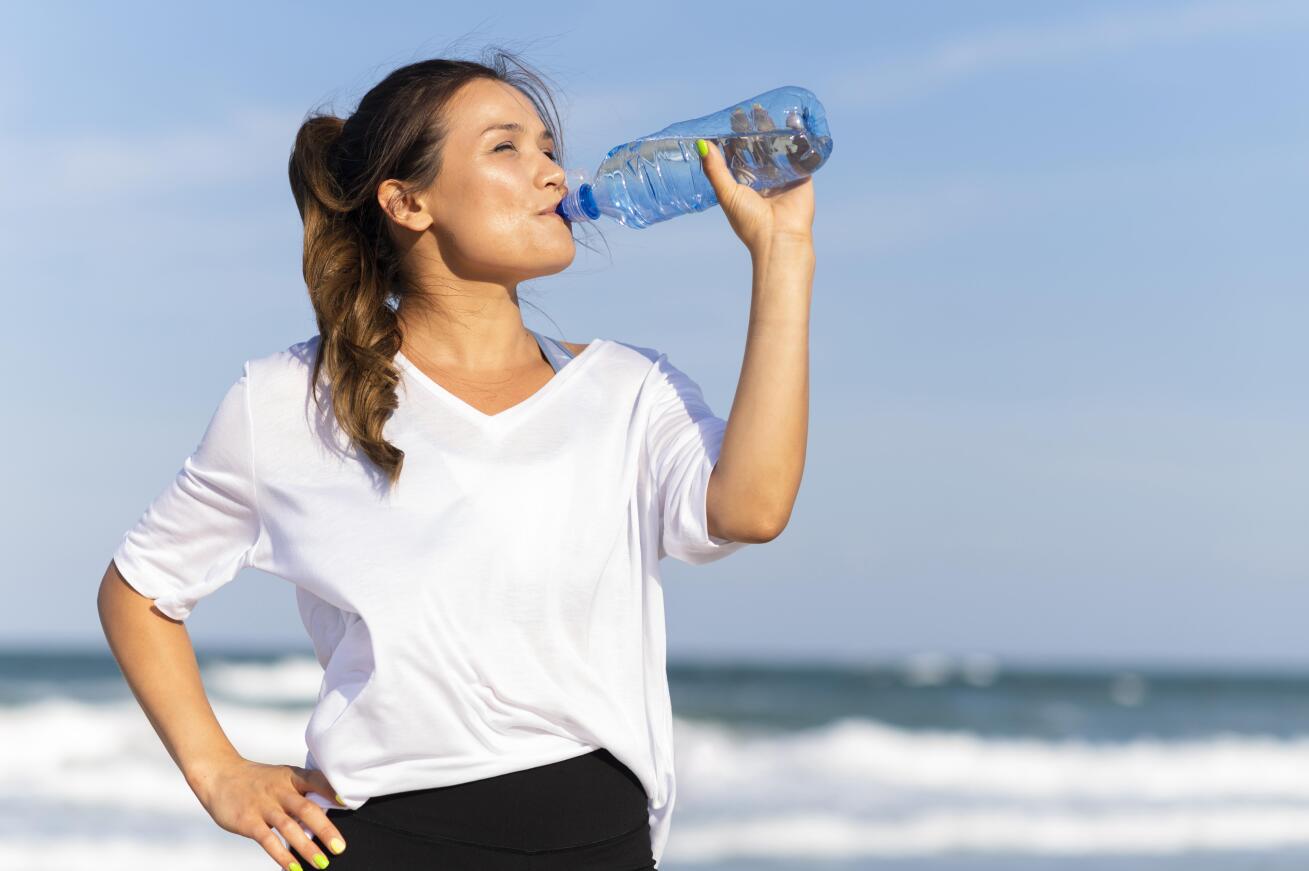 A young woman drinking water due to excess heat.