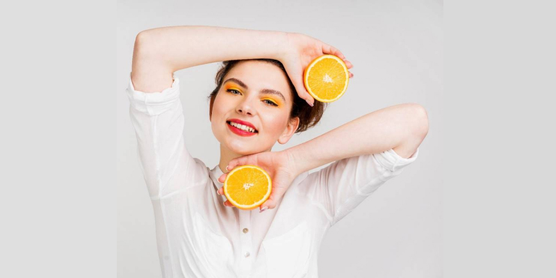 Image of a happy woman with cut oranges in hands illustrate vitamin C benefits.
