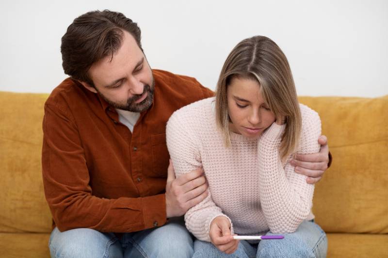 A couple with concerned expressions, glancing at a pregnancy test, highlighting the emotional impact of PCOS.