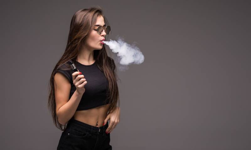 Young beautiful woman smoking ( vaping ) e-cigarette with smoke outdoors. 