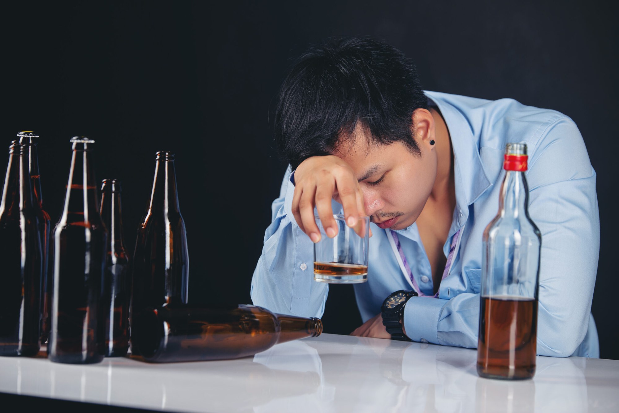 Sad man with a glass of alcohol and empty beer bottles, illustrating the health impacts of excessive drinking and premature aging.