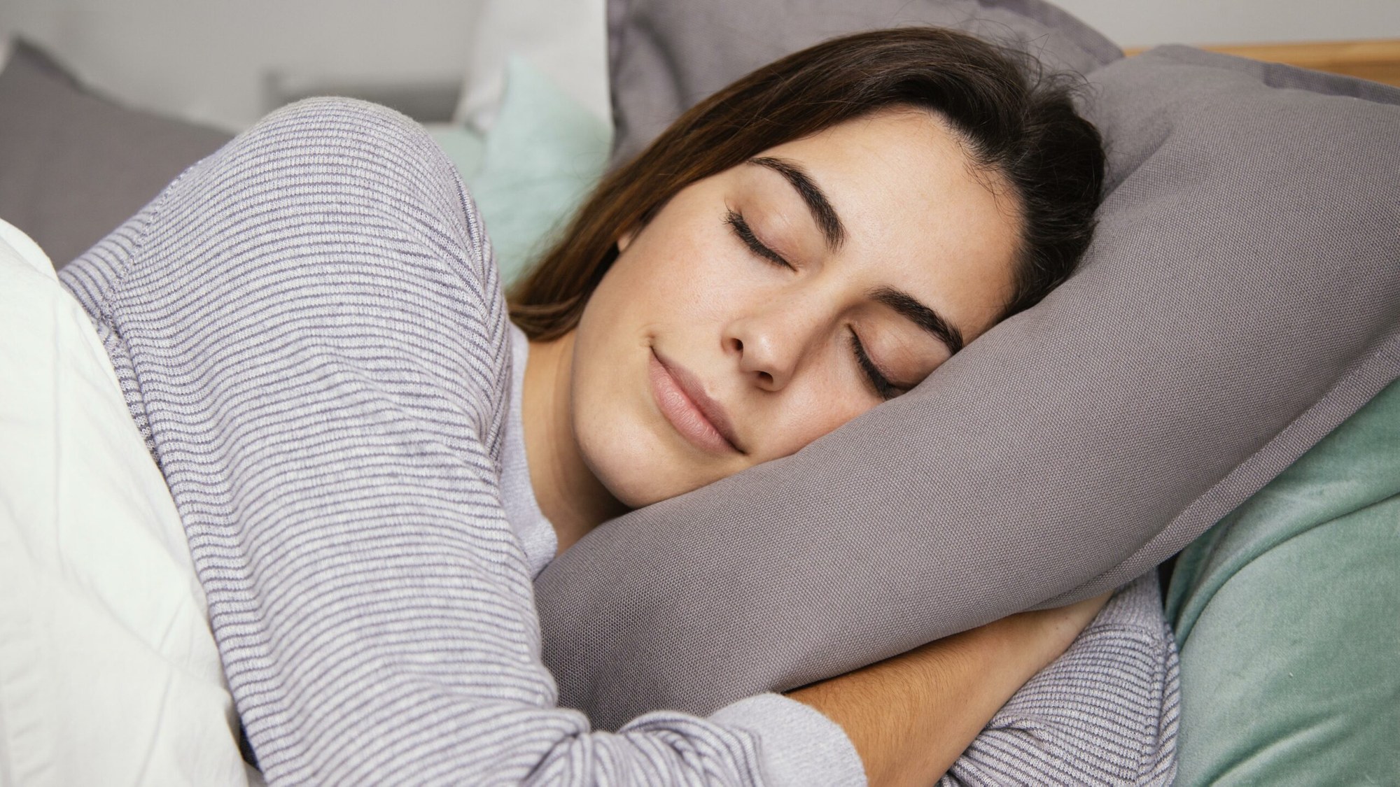 Peacefully sleeping woman in a comfortable bed, symbolizing the risks of side sleeping for skin health and premature aging.