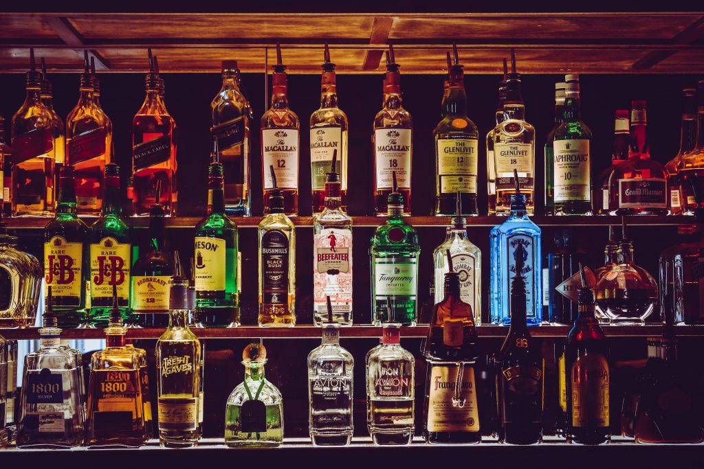 A bar shelf filled with liquor bottles, beautifully lit in the dark, with the bottles highlighted.