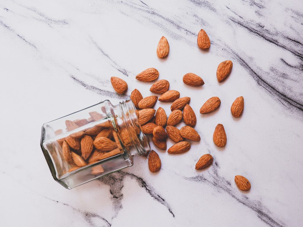 An aesthetic shot of almonds, a rich source of Vitamin E, spilling from a glass jar that is lying on the floor.