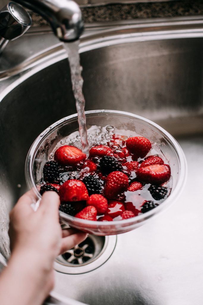 Assorted berries, known for their role in supporting heart health, being rinsed in a bowl under a tap.