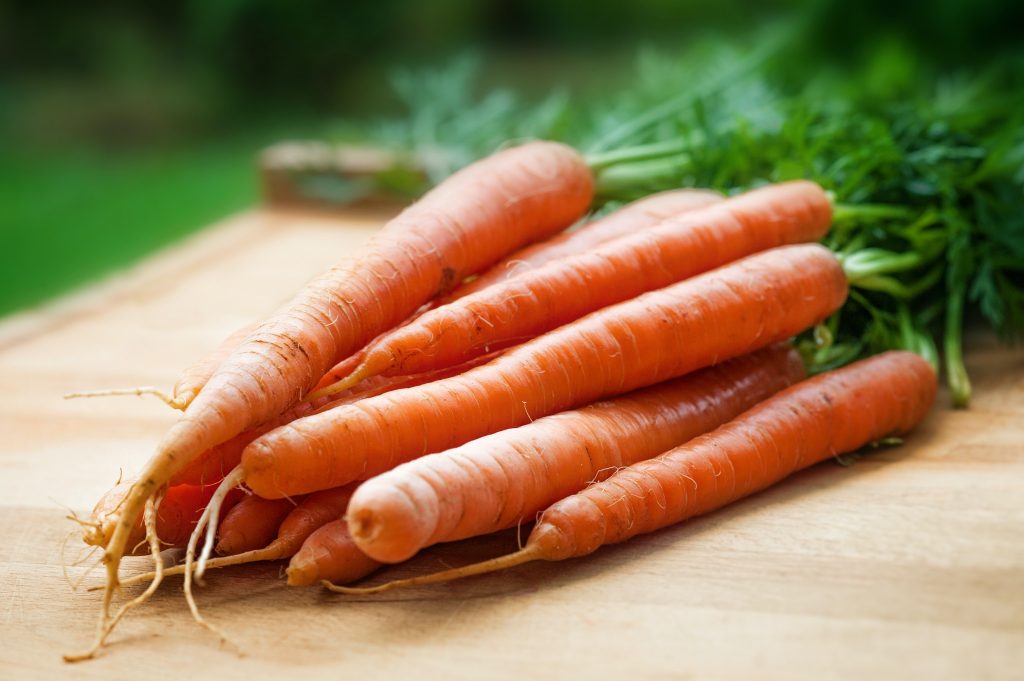 An exquisite image of garden-fresh carrots, rich in vitamin K, vitamin B6, magnesium, and beta carotene, neatly arranged on a wooden platter.