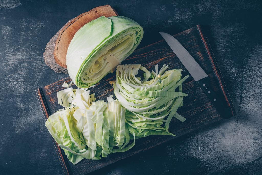 An aesthetic top view of a cabbage sliced in half, with the other half thinly sliced and a sharp knife placed nearby.