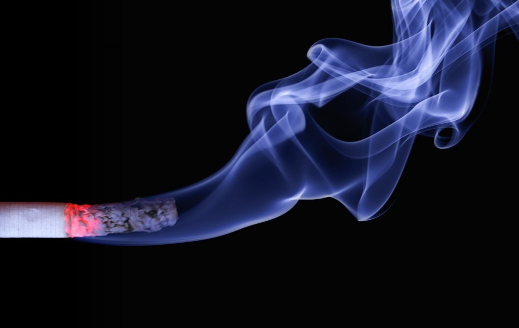 A striking image of a half-burnt cigarette emitting smoke against a black background, apossible reason for allergy. 