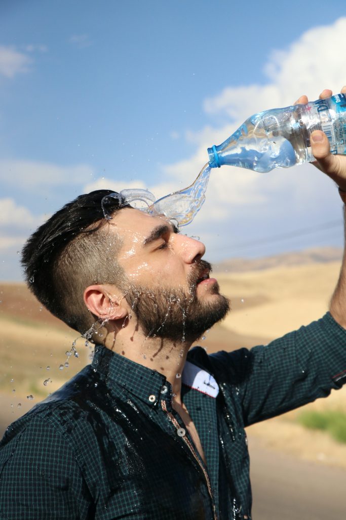 A man, dehydrated and fatigued, pouring water over his face from a water bottle to refresh himself.