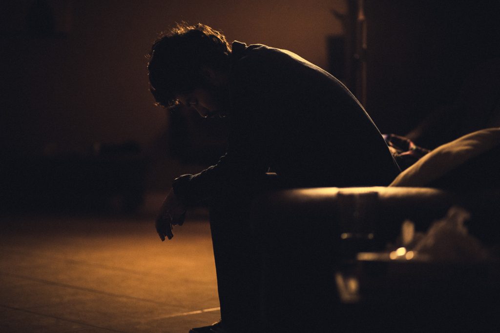 A man sitting on a couch in the dark, looking depressed and lost in thought.