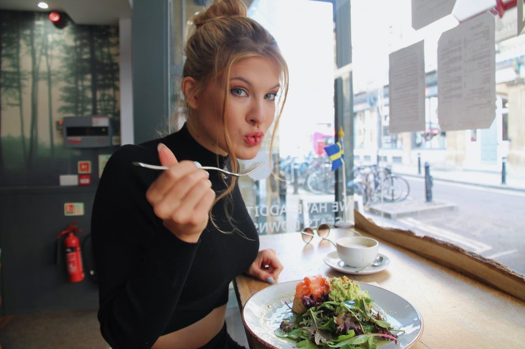 A stylish woman standing and eating with a fork, enjoying a meal with a cup of coffee, demonstrating healthy eating when dining out