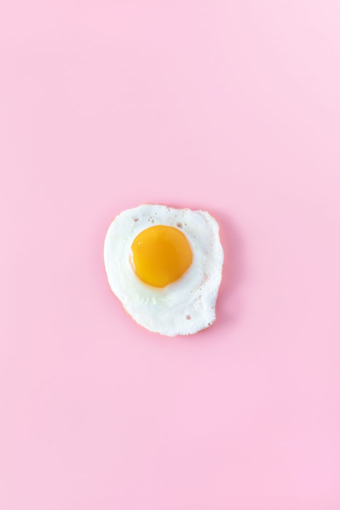 An aesthetic shot of a half-fried egg neatly presented on a pink surface, debunking the myth that eggs are bad for heart health.