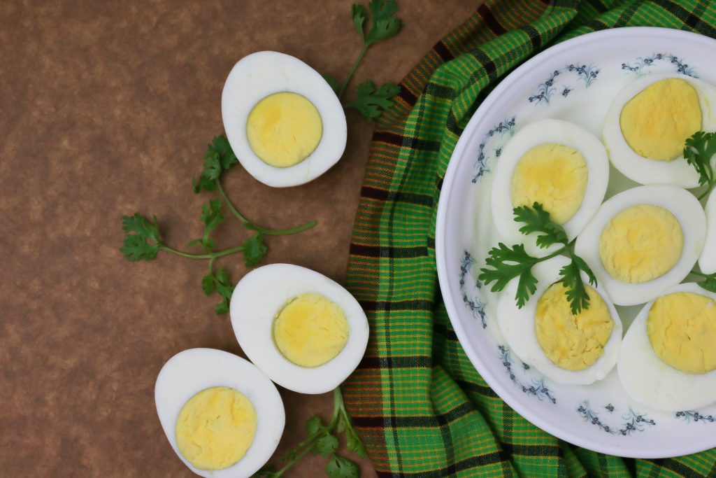 Half-sliced hard-boiled eggs with mint leaves on a white plate under a green cloth, showcasing a small healthy snack when eating out.