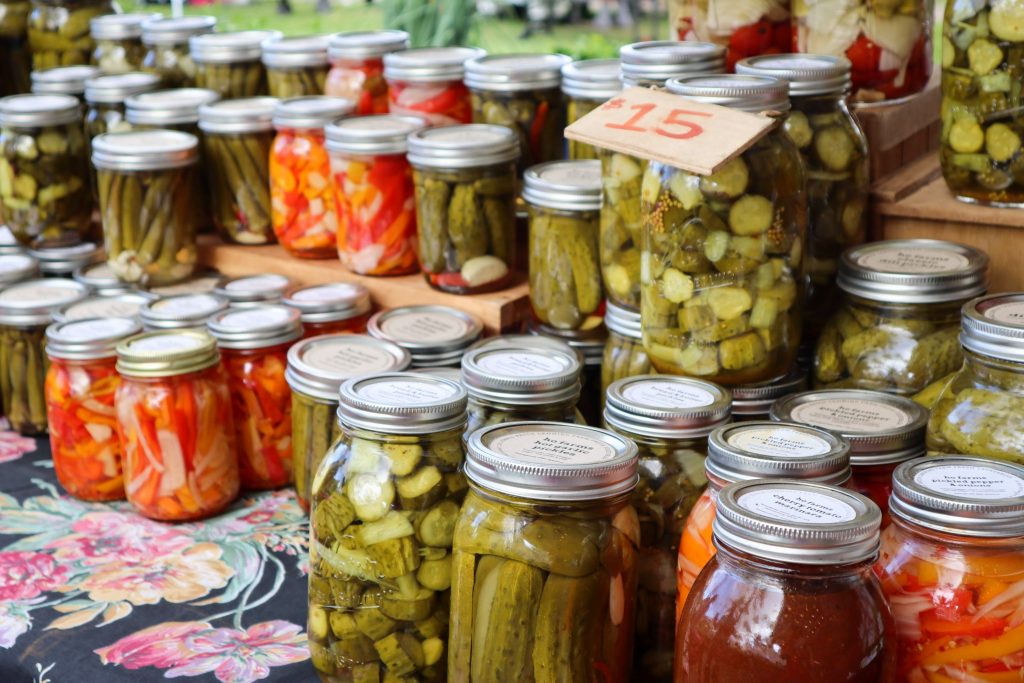 Glass jars filled with a variety of preserved vegetables, neatly displayed in a stall.