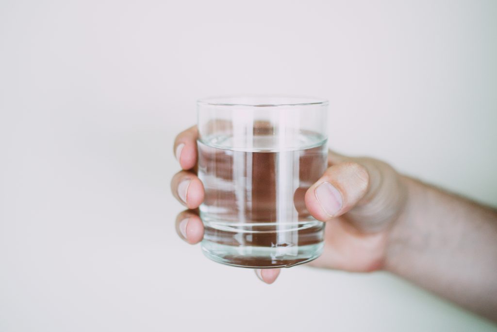 A person's hand holding a transparent glass of water, illustrating that excessive water intake can lead to hyponatremia.