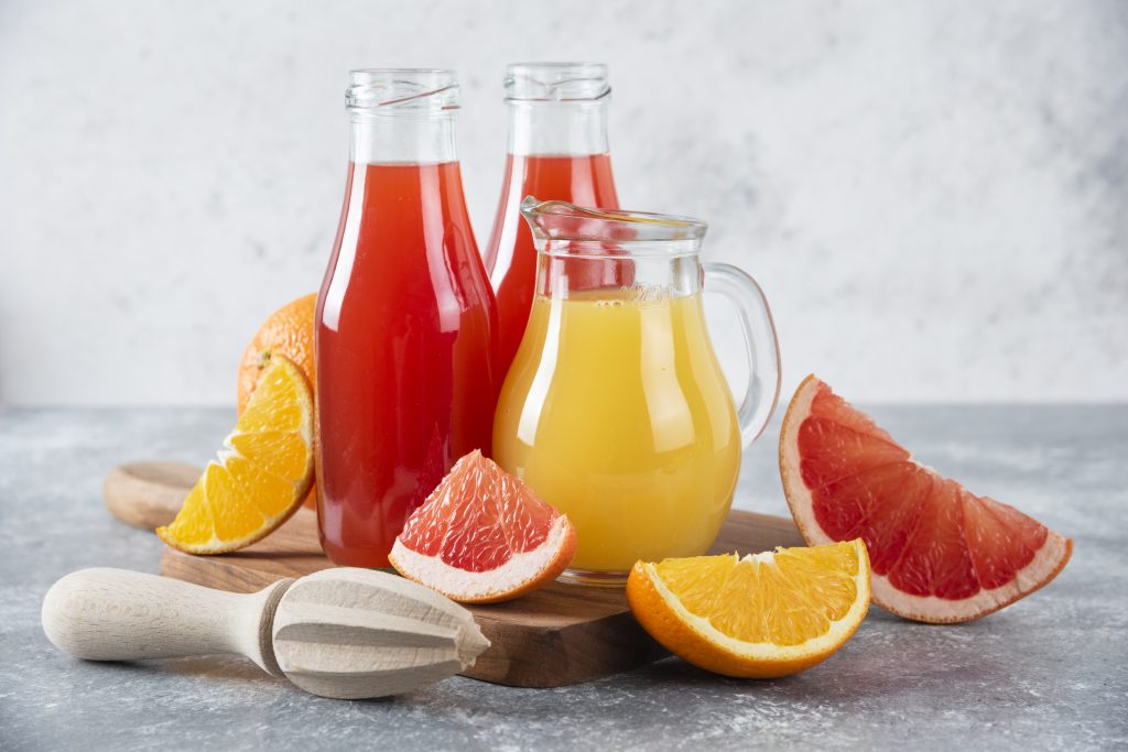 Fresh fruit juices in bottles and a jug with sliced citrus fruits on a wooden board, offering an alternative to water for hydration.