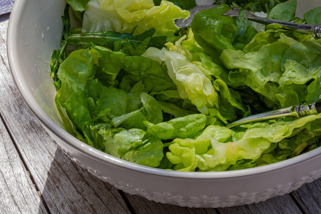 A bowl filled with fresh green salad, reminding us that enjoying greens early in the meal can lead to eating fewer and healthier portions overall.