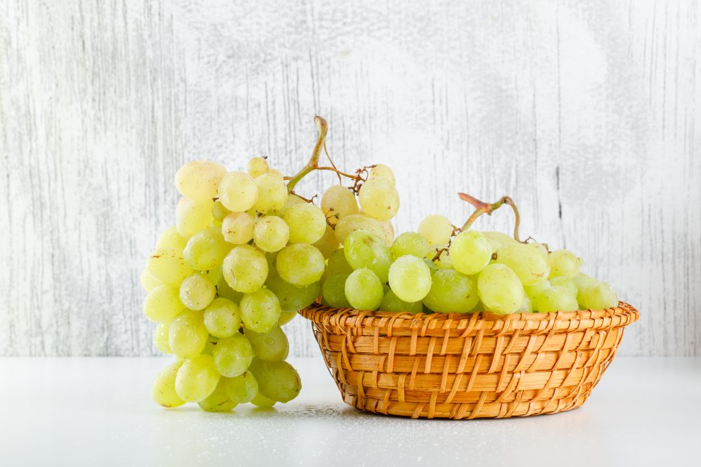 A bunch of green grapes arranged aesthetically in a basket on a white surface.