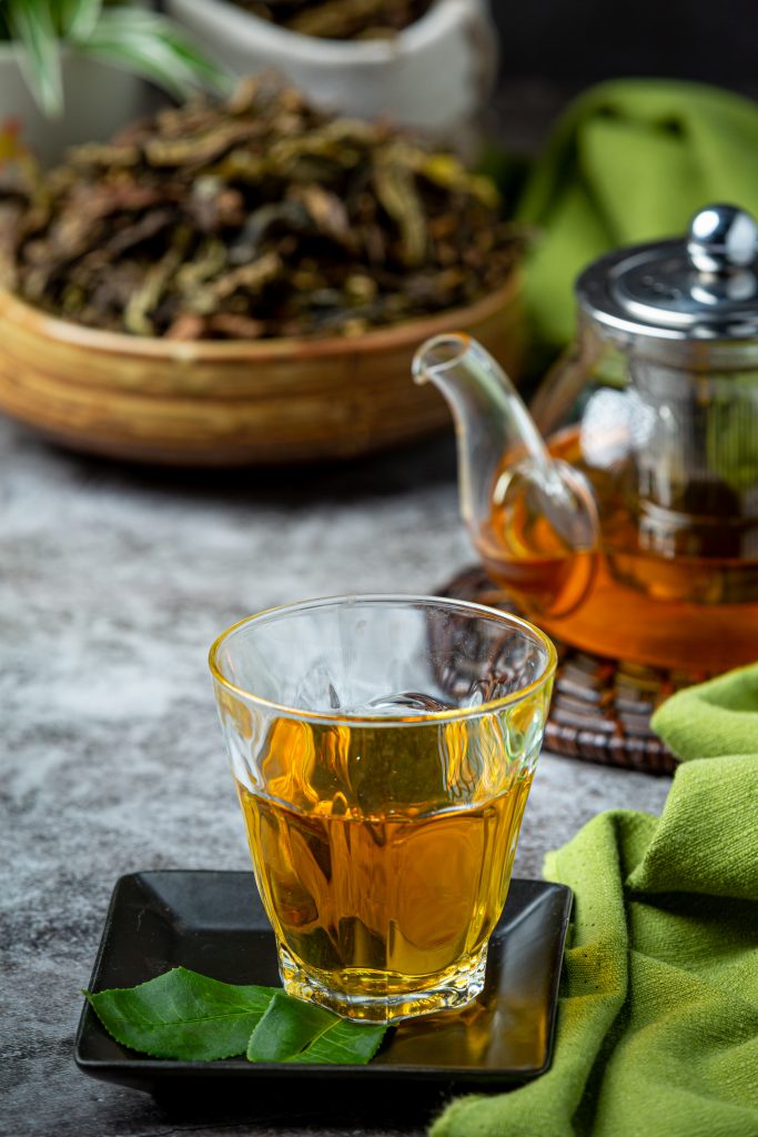 A glass of black tea placed on a table with a teapot nearby.