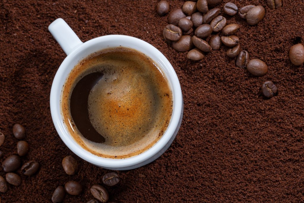 A top-view shot of a coffee-filled cup placed over a bed of coffee powder and scattered coffee beans.