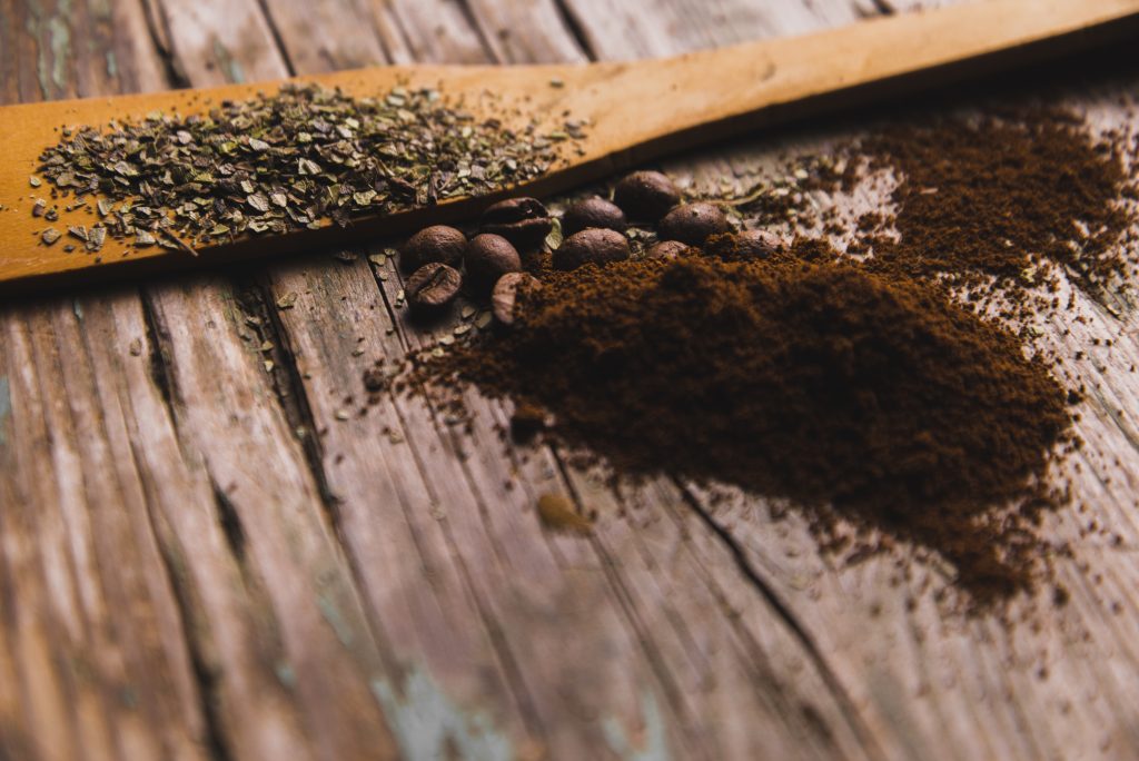Coffee grounds on a wooden surface, alongside coffee beans, highlighting their importance as an effective fertilizer.