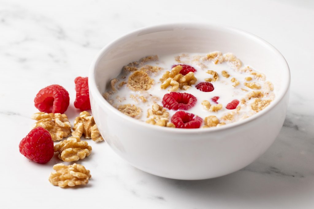A bowl of cereals in milk, topped with strawberries and walnuts.