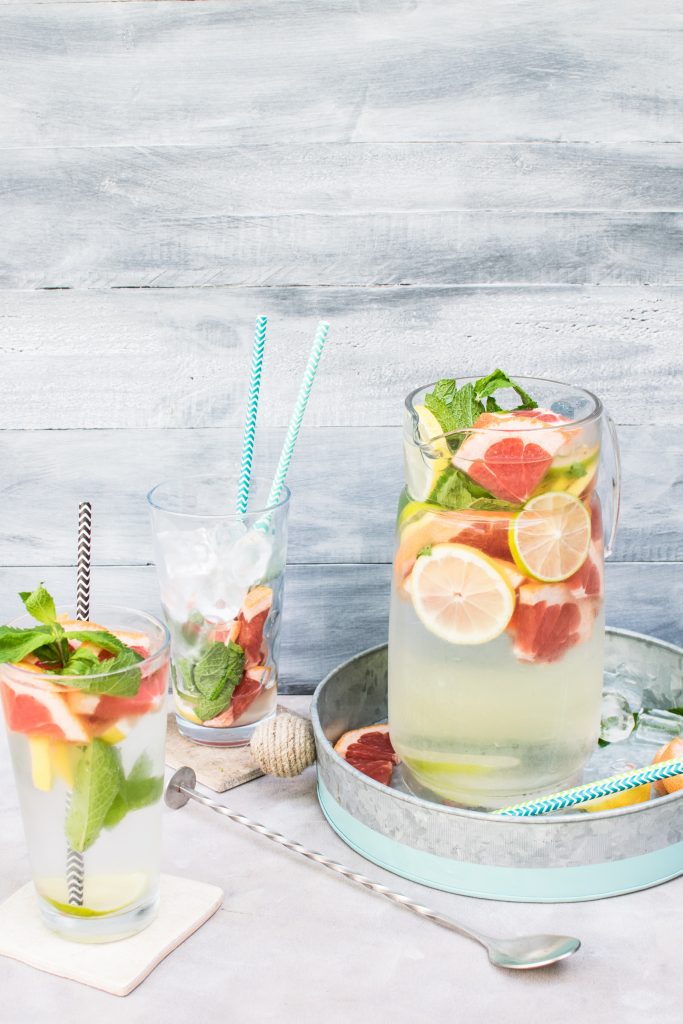 Peels of citrus fruits, apples, and cucumbers infused in water inside glass jars, topped with herbs for a refreshing taste.