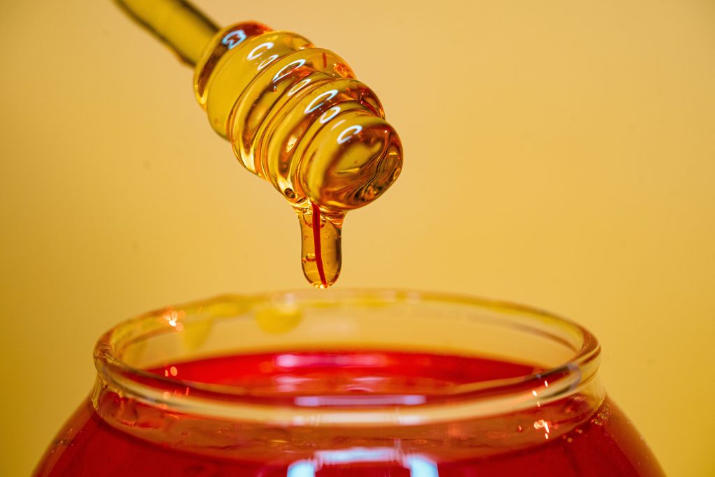 A stunning image of raw honey, highlighting its antimicrobial and anti-inflammatory properties, dripping from a wooden honey dipper.