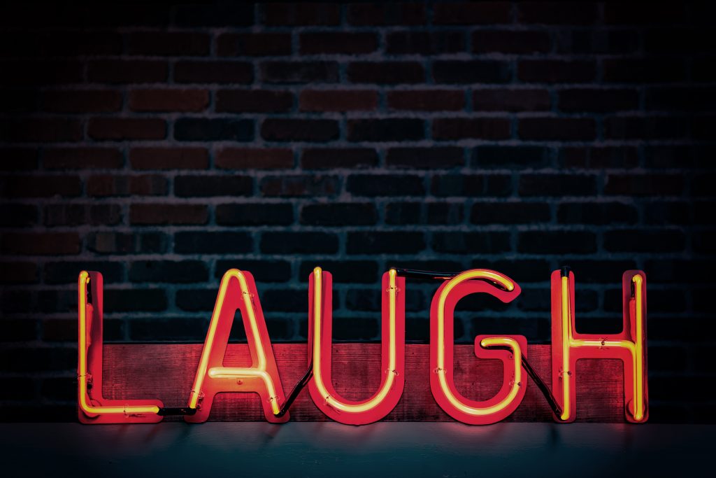Orange neon lights arranged to spell 'LAUGH' outside a building, highlighting the power of laughter in reducing stress."