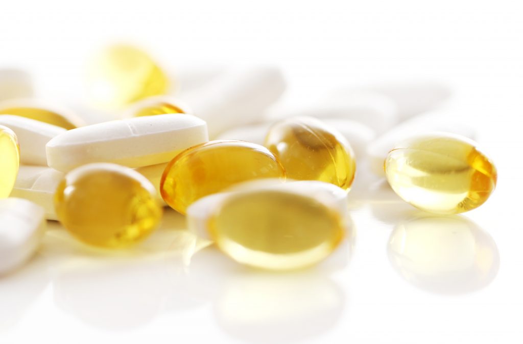 Assorted pills, including calcium and omega-3 fatty acids, spilled on a white surface.