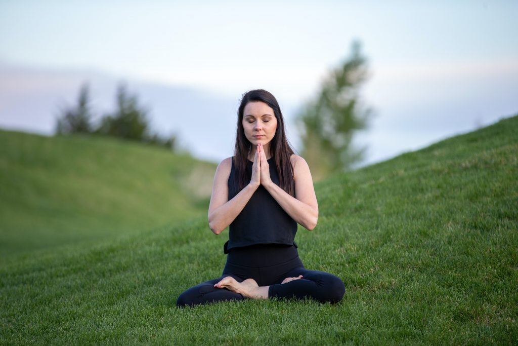 A woman peacefully sitting and meditating in a green meadow.