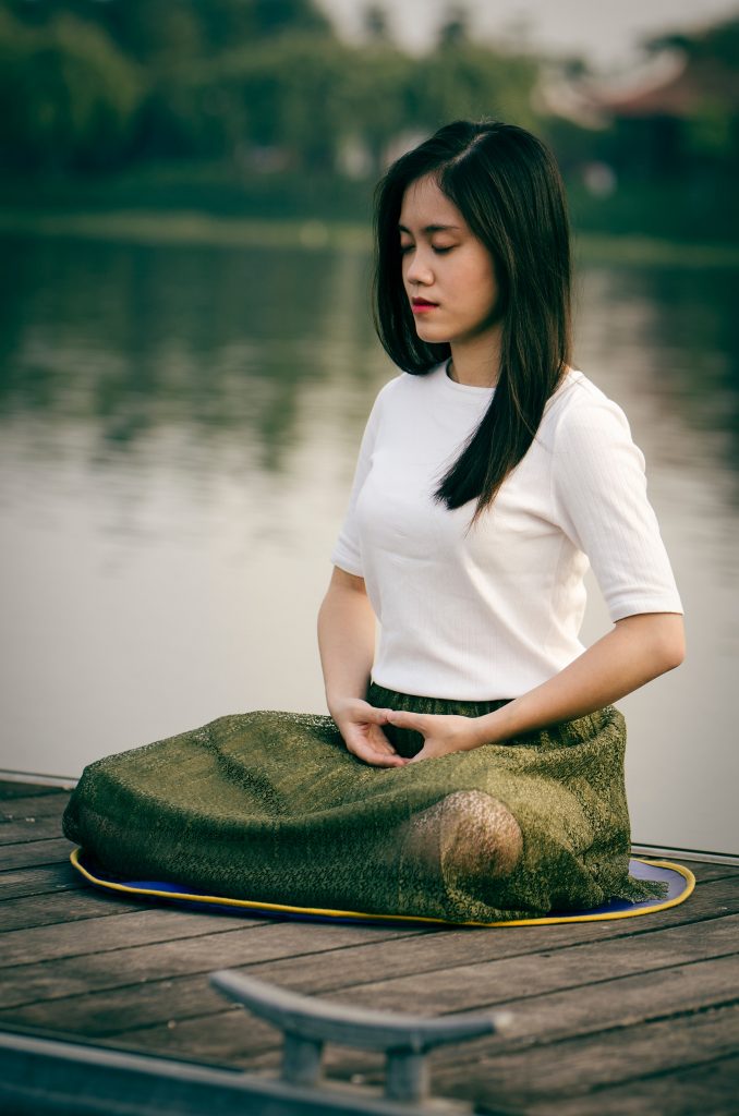 A young Asian woman meditating outdoors, highlighting the role of meditation in alleviating anxiety symptoms.